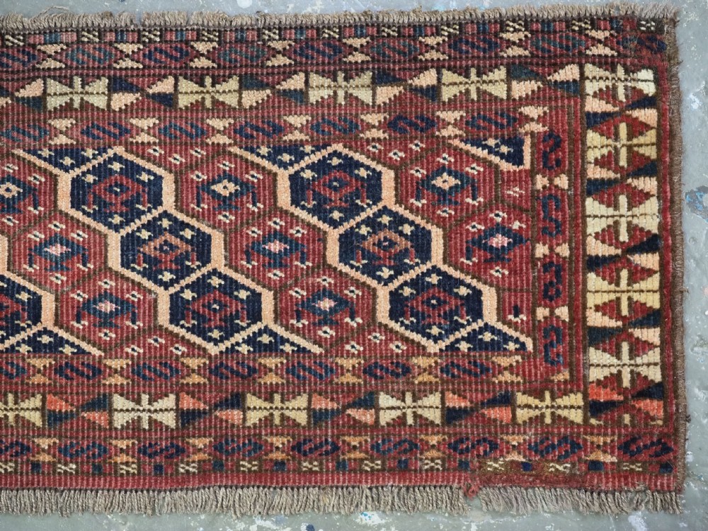 A horizontal woven antique Turkmen torba panel in deep terracotta red, navy blue, and cream, featuring repeating geometric octagonal Schemle gul motifs across the field. View IV