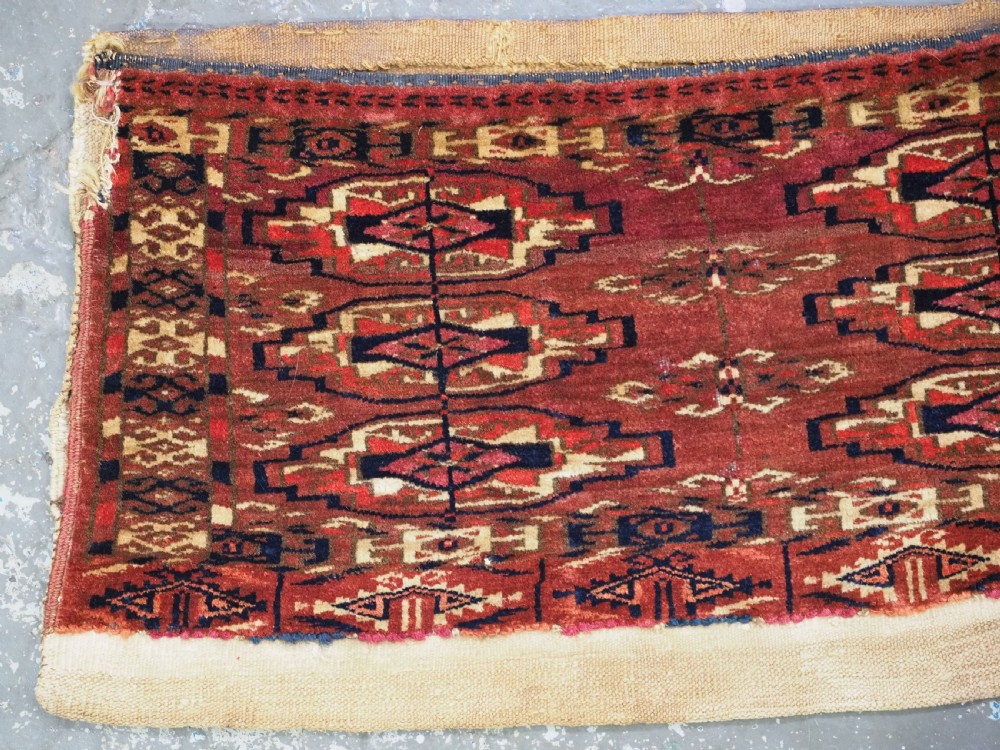 A small rectangular 19th-century Tekke Turkmen wool torba featuring nine geometric guls on a deep red field with an attached cream wool backing. View II