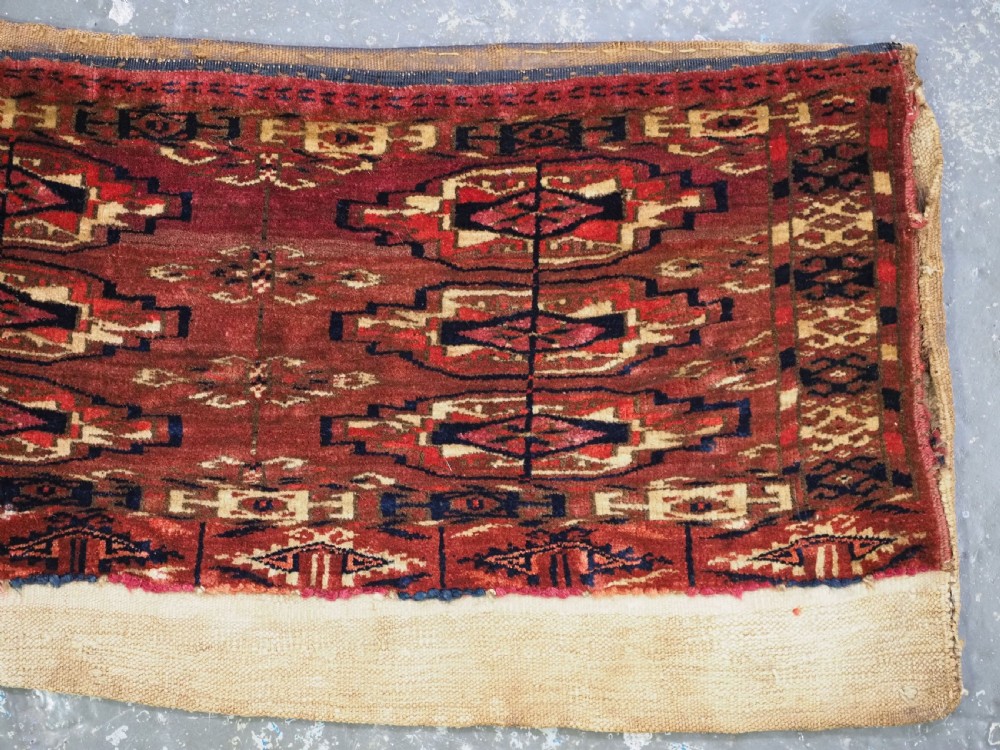 A small rectangular 19th-century Tekke Turkmen wool torba featuring nine geometric guls on a deep red field with an attached cream wool backing. View IV