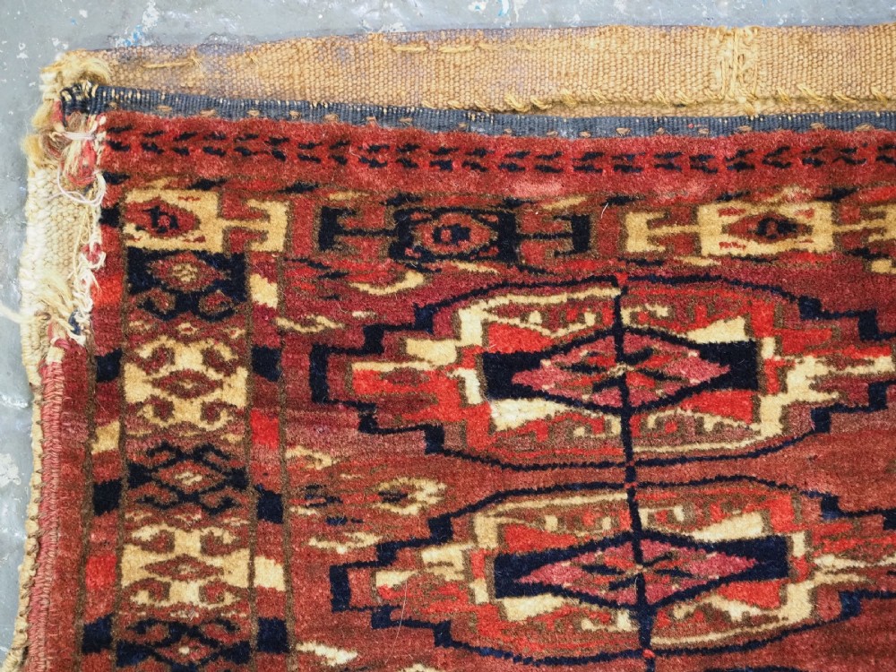 A small rectangular 19th-century Tekke Turkmen wool torba featuring nine geometric guls on a deep red field with an attached cream wool backing. View VI