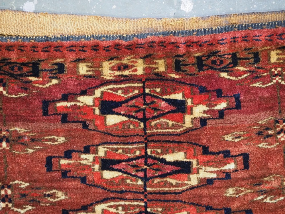 A small rectangular 19th-century Tekke Turkmen wool torba featuring nine geometric guls on a deep red field with an attached cream wool backing. View VII