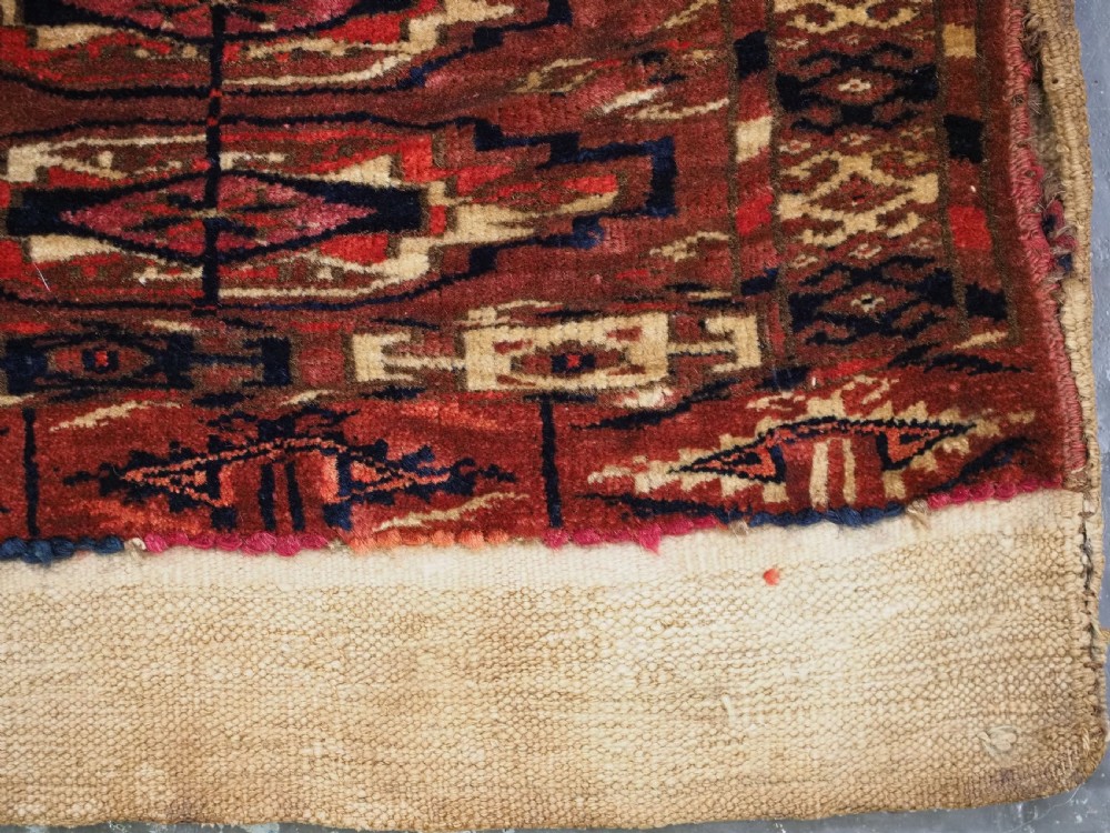 A small rectangular 19th-century Tekke Turkmen wool torba featuring nine geometric guls on a deep red field with an attached cream wool backing. View VIII