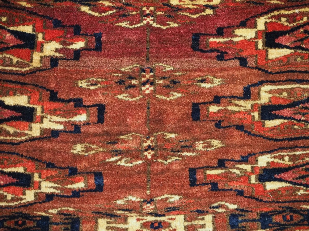 A small rectangular 19th-century Tekke Turkmen wool torba featuring nine geometric guls on a deep red field with an attached cream wool backing. View X