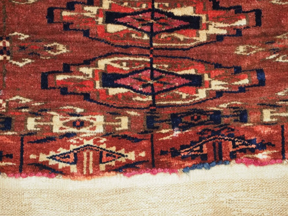 A small rectangular 19th-century Tekke Turkmen wool torba featuring nine geometric guls on a deep red field with an attached cream wool backing. View XI