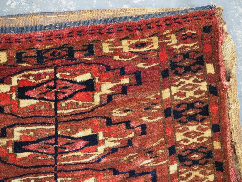 A small rectangular 19th-century Tekke Turkmen wool torba featuring nine geometric guls on a deep red field with an attached cream wool backing. View XII
