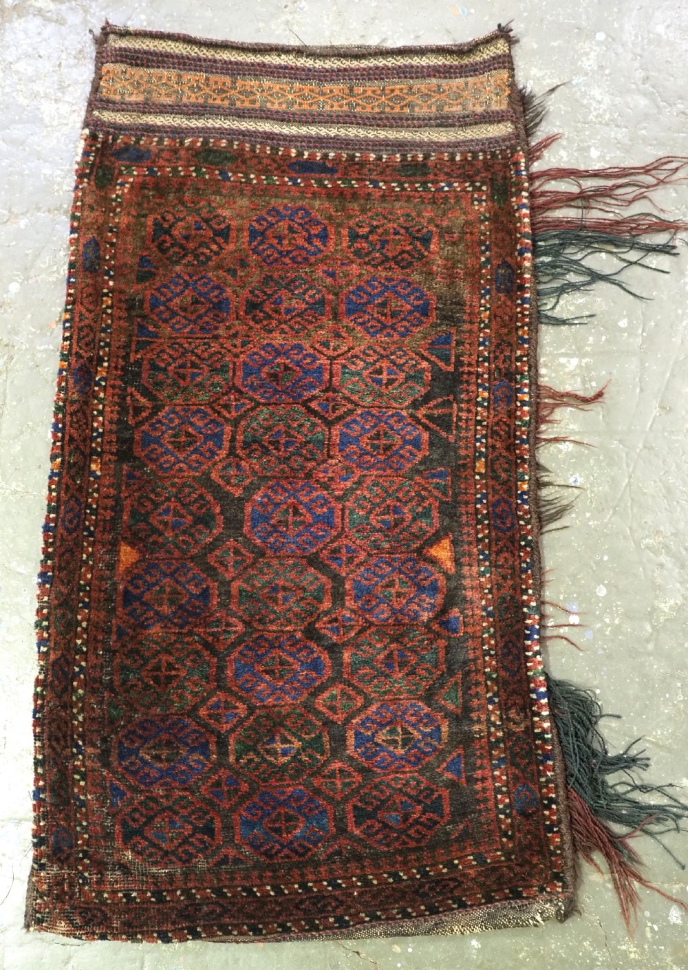An antique woven Baluch Balisht storage bag featuring dark red and navy blue geometric octagonal motifs with a flat-weave top border and fringed edges.