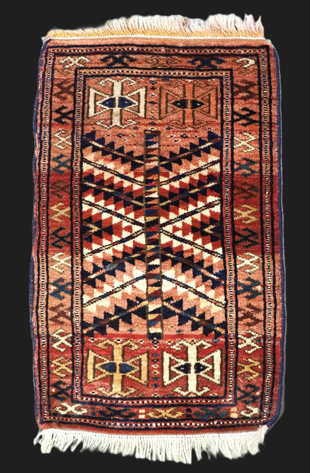 An antique hand-knotted Yomut Turkmen woven bag face featuring intricate geometric serrated motifs in terracotta, navy, and cream with fringed borders.