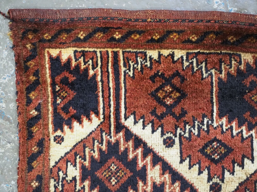 An antique rectangular Ersari Turkmen torba bag face featuring geometric curled leaf motifs in navy blue and terracotta red on an ivory background with fringed trim. View V