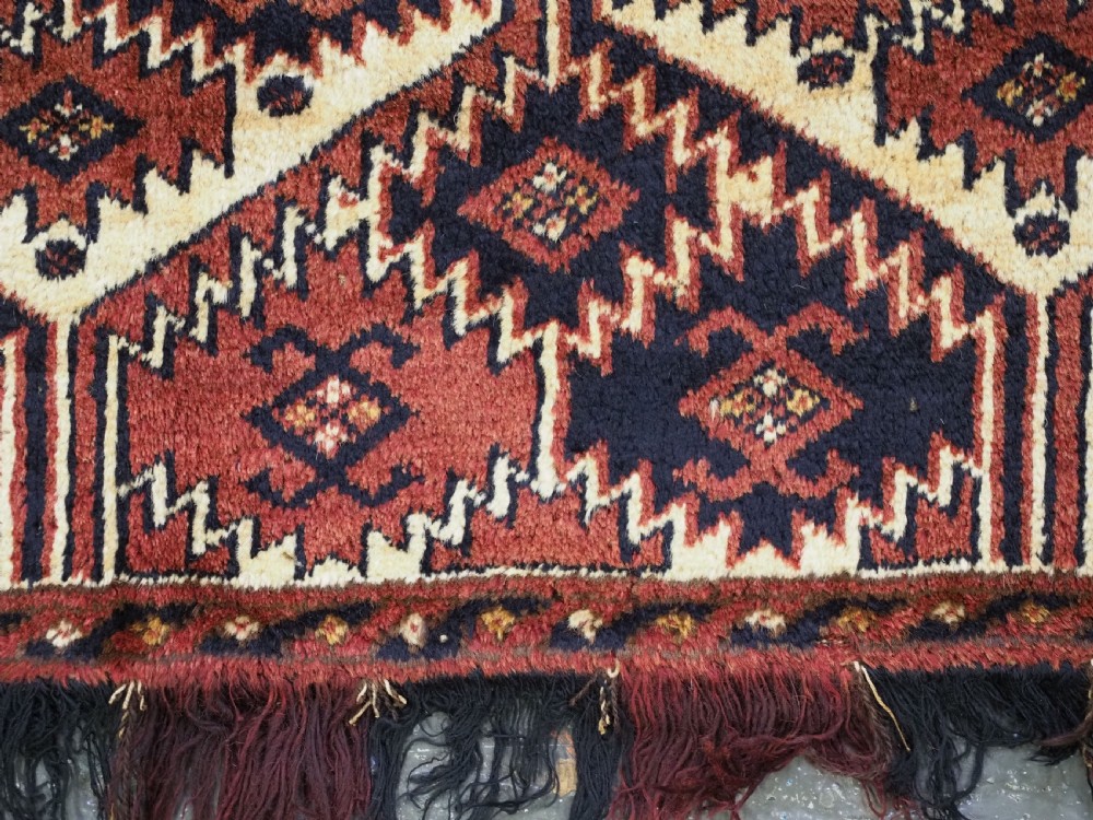 An antique rectangular Ersari Turkmen torba bag face featuring geometric curled leaf motifs in navy blue and terracotta red on an ivory background with fringed trim. View X