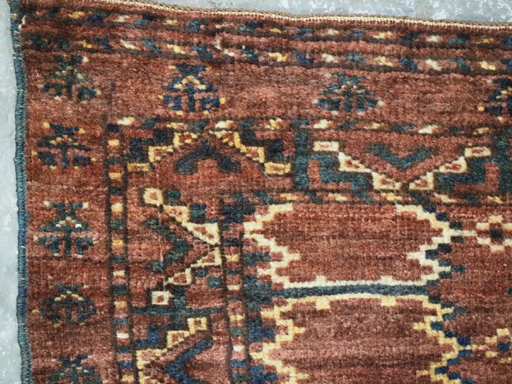A horizontal hand-knotted antique wool torba displaying a repeating ikat diamond pattern in terracotta red, navy blue, and ochre hues. View IV