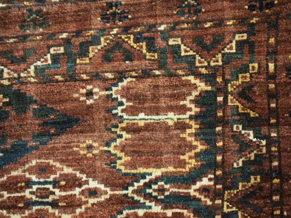A horizontal hand-knotted antique wool torba displaying a repeating ikat diamond pattern in terracotta red, navy blue, and ochre hues. View VII