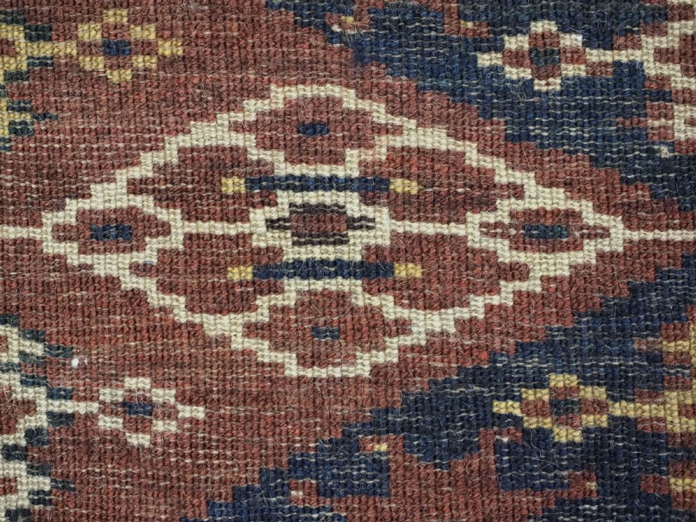 A horizontal hand-knotted antique wool torba displaying a repeating ikat diamond pattern in terracotta red, navy blue, and ochre hues. View VIII