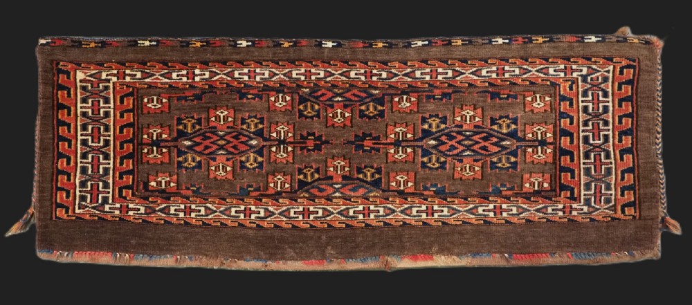 A horizontal rectangular handwoven wool Turkmen torba bag featuring geometric Kepse gul motifs in red and navy on a dark brown ground.