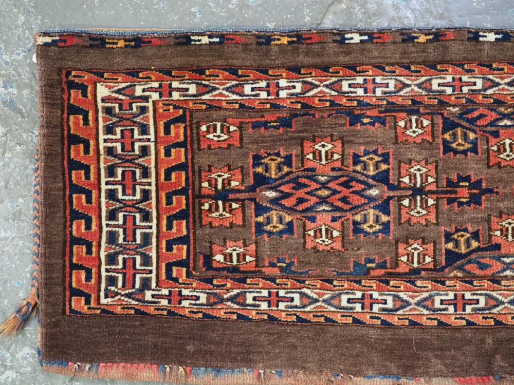A horizontal rectangular handwoven wool Turkmen torba bag featuring geometric Kepse gul motifs in red and navy on a dark brown ground. View II