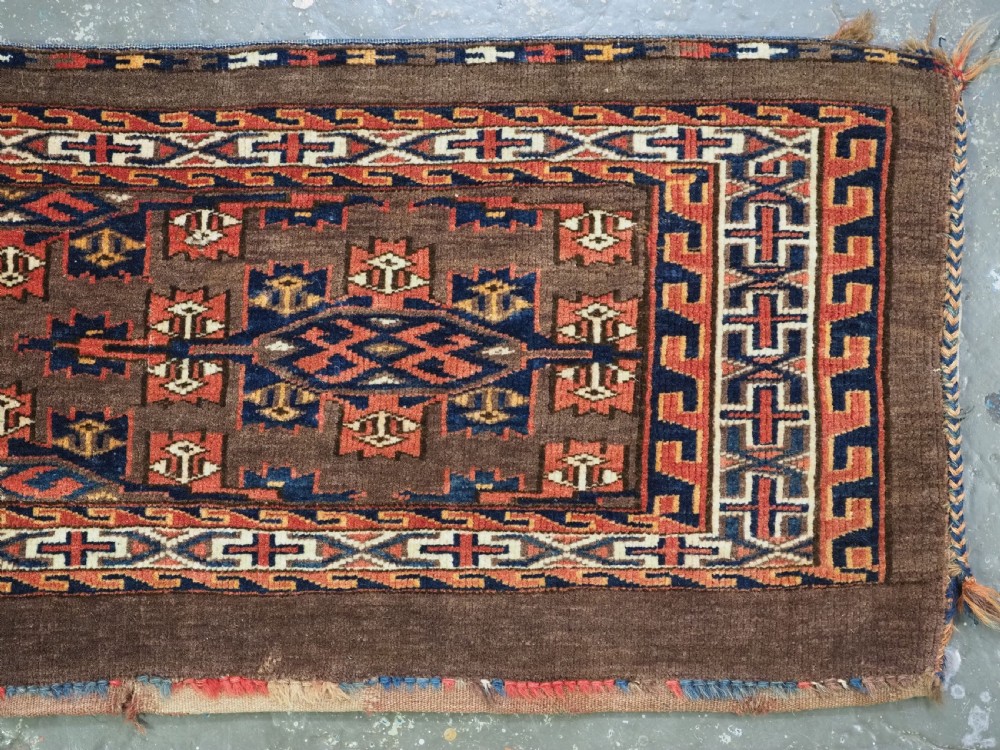 A horizontal rectangular handwoven wool Turkmen torba bag featuring geometric Kepse gul motifs in red and navy on a dark brown ground. View IV