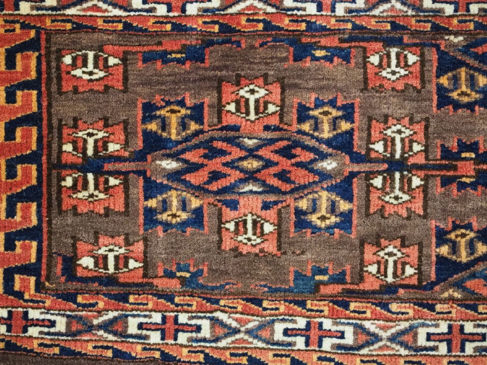 A horizontal rectangular handwoven wool Turkmen torba bag featuring geometric Kepse gul motifs in red and navy on a dark brown ground. View V