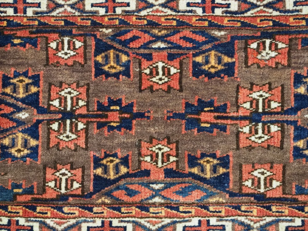 A horizontal rectangular handwoven wool Turkmen torba bag featuring geometric Kepse gul motifs in red and navy on a dark brown ground. View VI