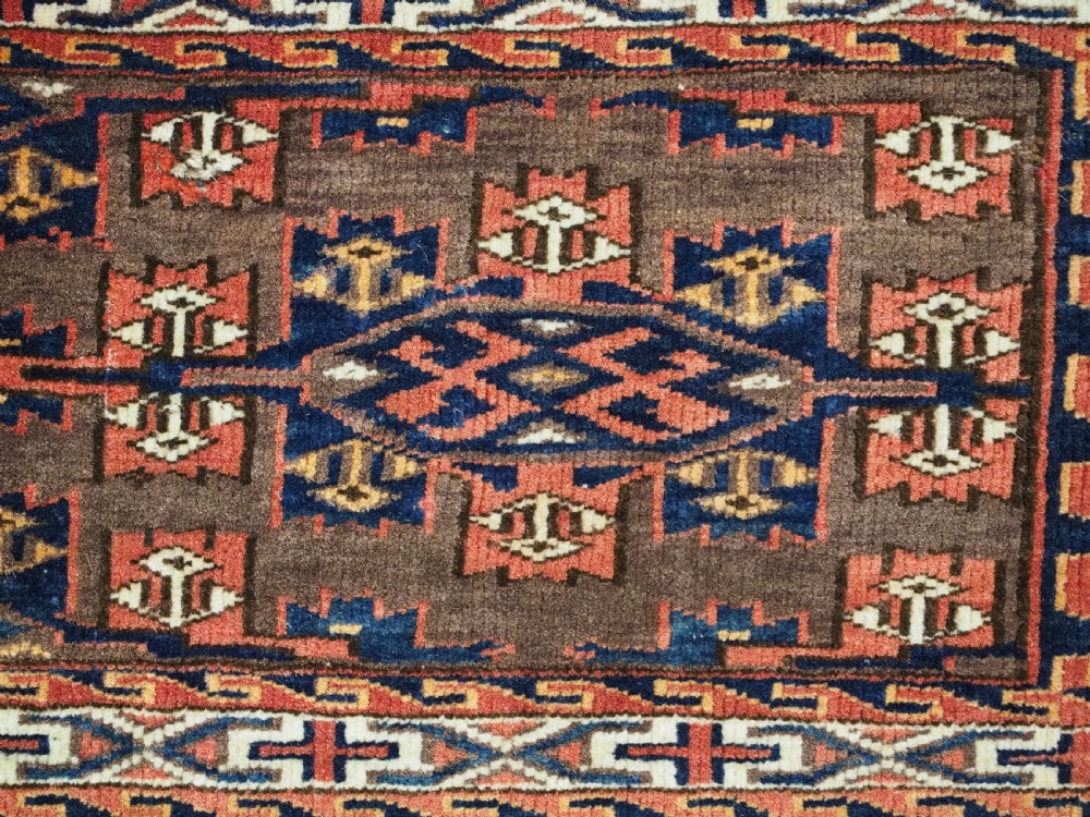 A horizontal rectangular handwoven wool Turkmen torba bag featuring geometric Kepse gul motifs in red and navy on a dark brown ground. View VII