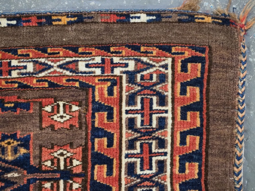 A horizontal rectangular handwoven wool Turkmen torba bag featuring geometric Kepse gul motifs in red and navy on a dark brown ground. View VIII