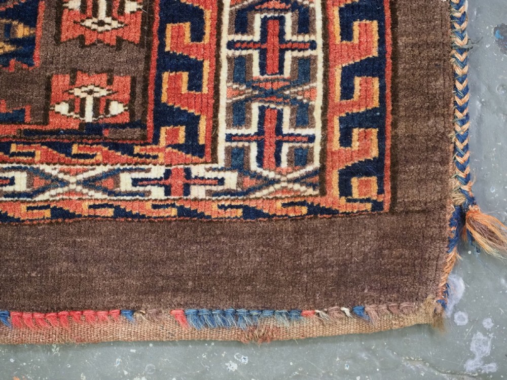 A horizontal rectangular handwoven wool Turkmen torba bag featuring geometric Kepse gul motifs in red and navy on a dark brown ground. View IX