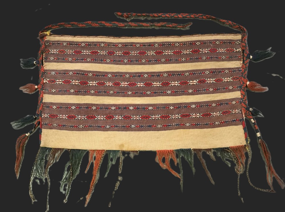 An antique Turkmen flatweave panel with horizontal cream, dark brown, and terracotta geometric bands decorated with side tassels and fringing.