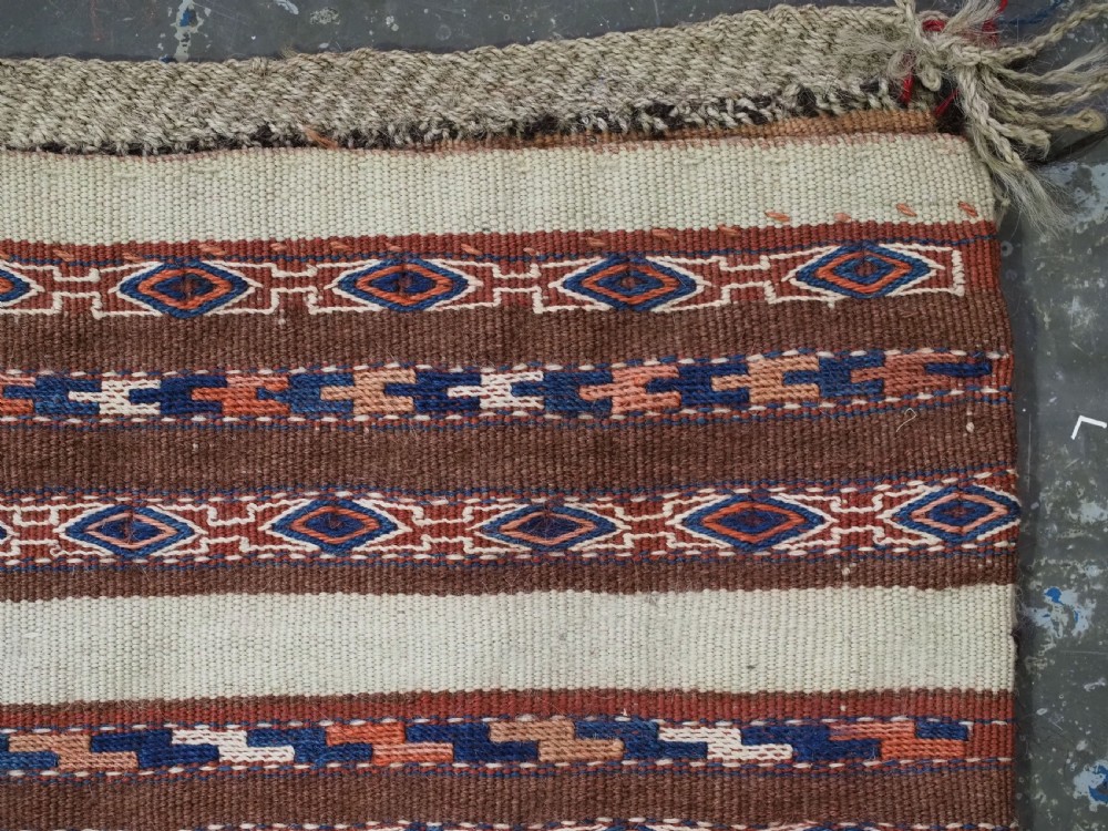 An antique hand-woven Turkmen flatweave textile panel featuring horizontal bands of geometric motifs in terracotta, dark blue, and brown on a cream background with long fringed trim. View VII
