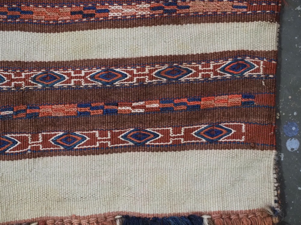 An antique hand-woven Turkmen flatweave textile panel featuring horizontal bands of geometric motifs in terracotta, dark blue, and brown on a cream background with long fringed trim. View VIII