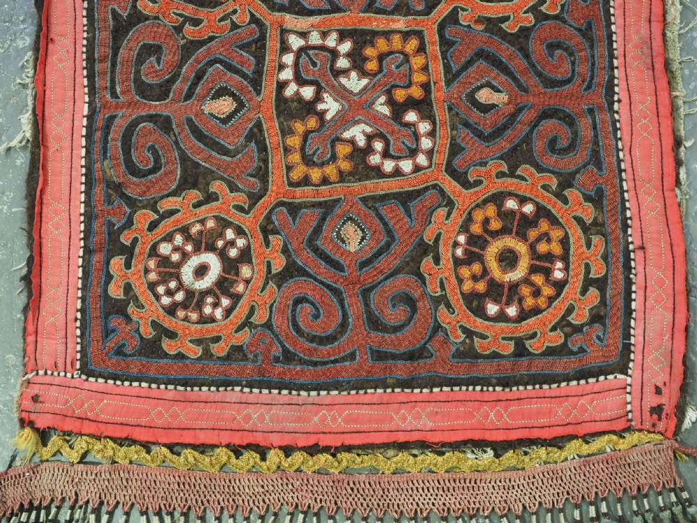 An antique square Kirghiz felt panel featuring central scroll embroidery in red, yellow, and white, framed by a red border with applied tasselled fringe at the bottom edge. View II