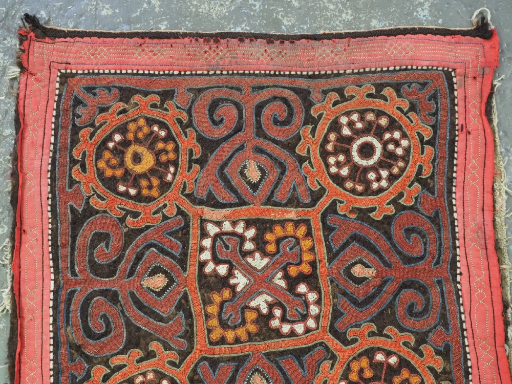 An antique square Kirghiz felt panel featuring central scroll embroidery in red, yellow, and white, framed by a red border with applied tasselled fringe at the bottom edge. View IV