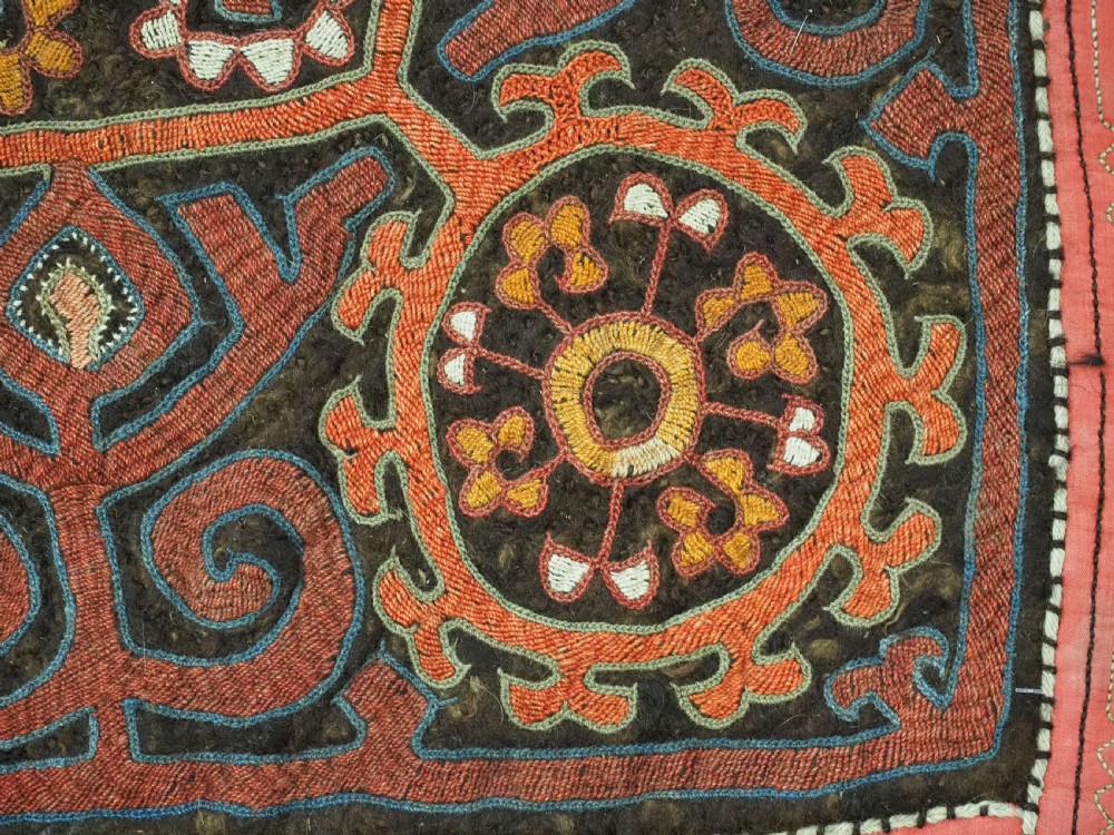 An antique square Kirghiz felt panel featuring central scroll embroidery in red, yellow, and white, framed by a red border with applied tasselled fringe at the bottom edge. View V