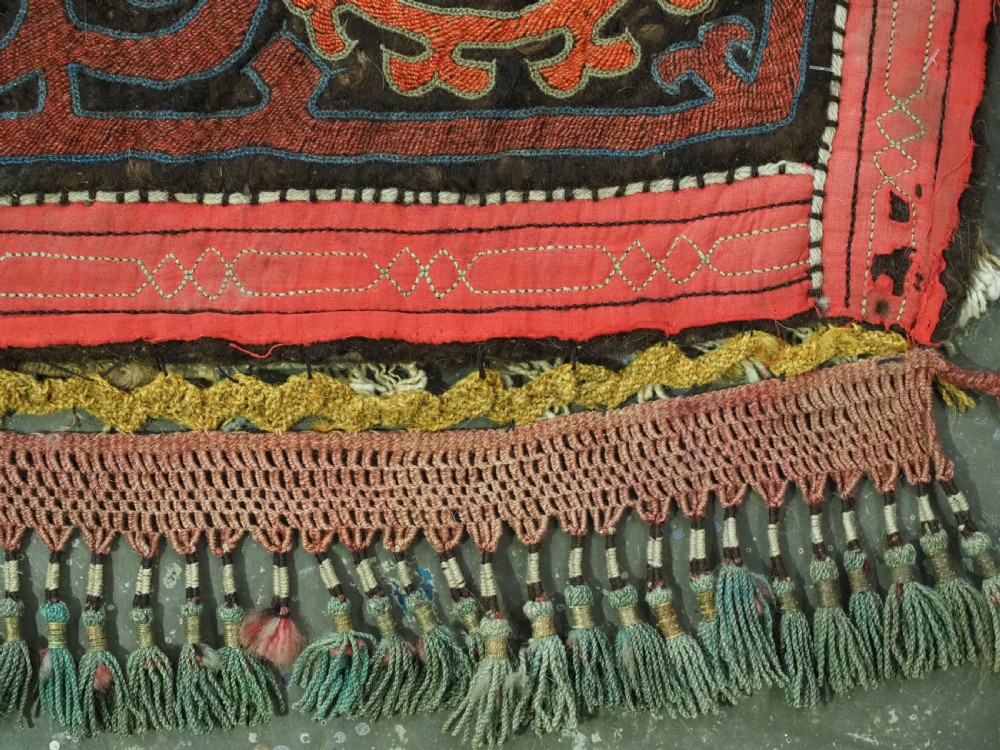 An antique square Kirghiz felt panel featuring central scroll embroidery in red, yellow, and white, framed by a red border with applied tasselled fringe at the bottom edge. View VI