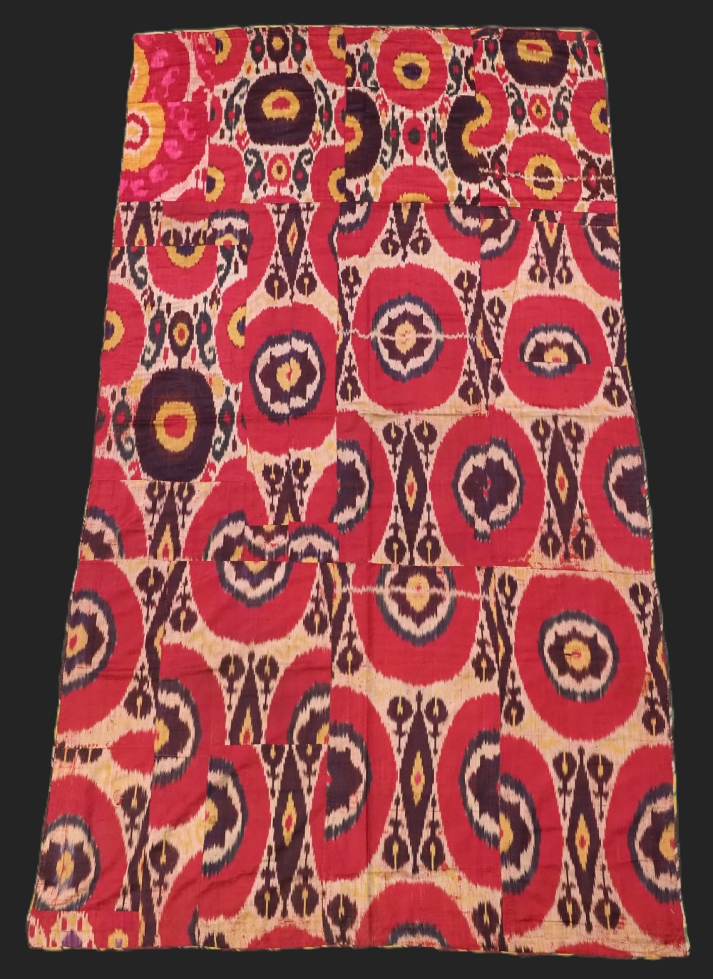 A vertical handwoven silk ikat textile panel featuring bold crimson, yellow, and deep purple circular geometric patterns on an off-white background.