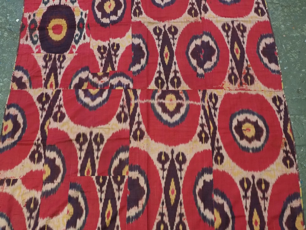 A vertical handwoven silk ikat textile panel featuring bold crimson, yellow, and deep purple circular geometric patterns on an off-white background. View V