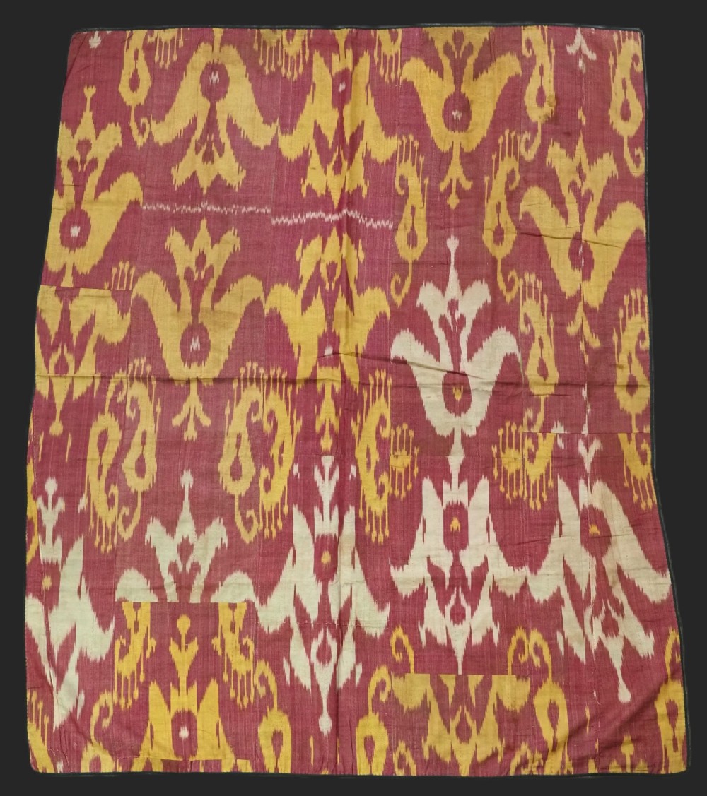 An antique Uzbek silk adras ikat panel featuring bold floral and geometric motifs in crimson red, mustard yellow, and cream.