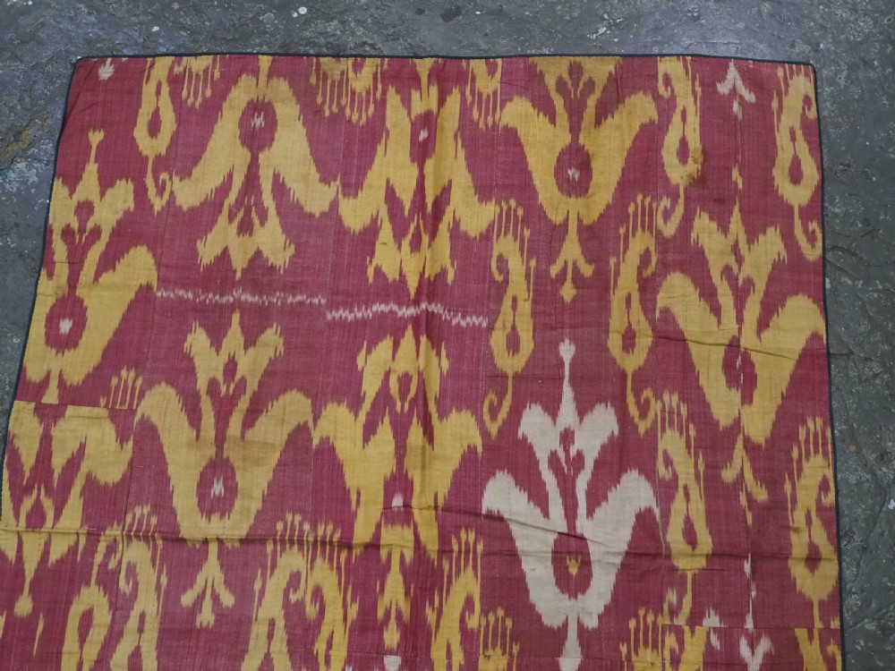 An antique Uzbek silk adras ikat panel featuring bold floral and geometric motifs in crimson red, mustard yellow, and cream. View III