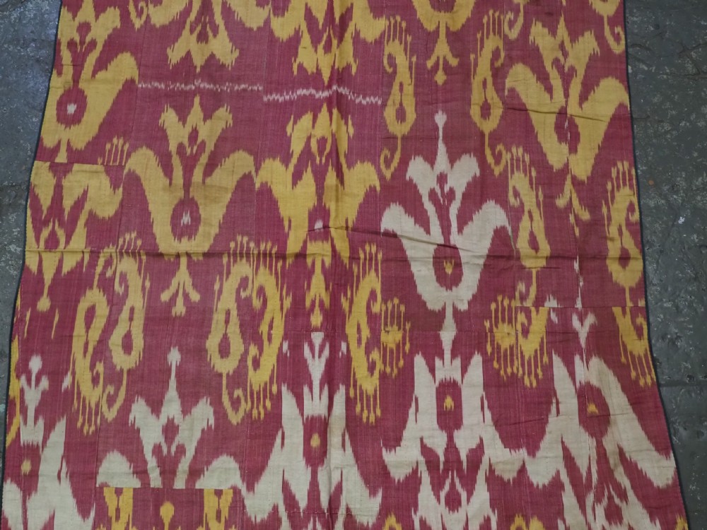 An antique Uzbek silk adras ikat panel featuring bold floral and geometric motifs in crimson red, mustard yellow, and cream. View IV