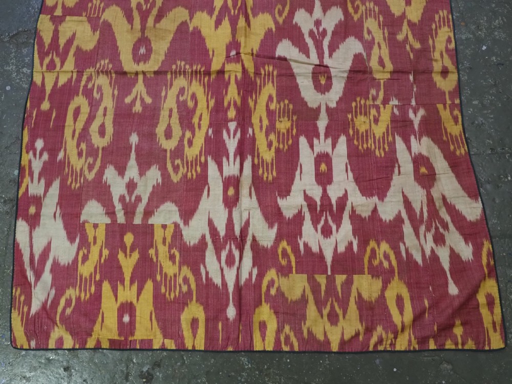 An antique Uzbek silk adras ikat panel featuring bold floral and geometric motifs in crimson red, mustard yellow, and cream. View V
