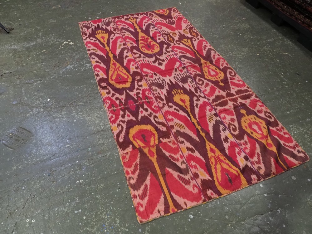 A rectangular handwoven Central Asian textile displaying vibrant geometric ikat motifs in crimson, yellow, and deep purple across three vertically stitched panels. View II