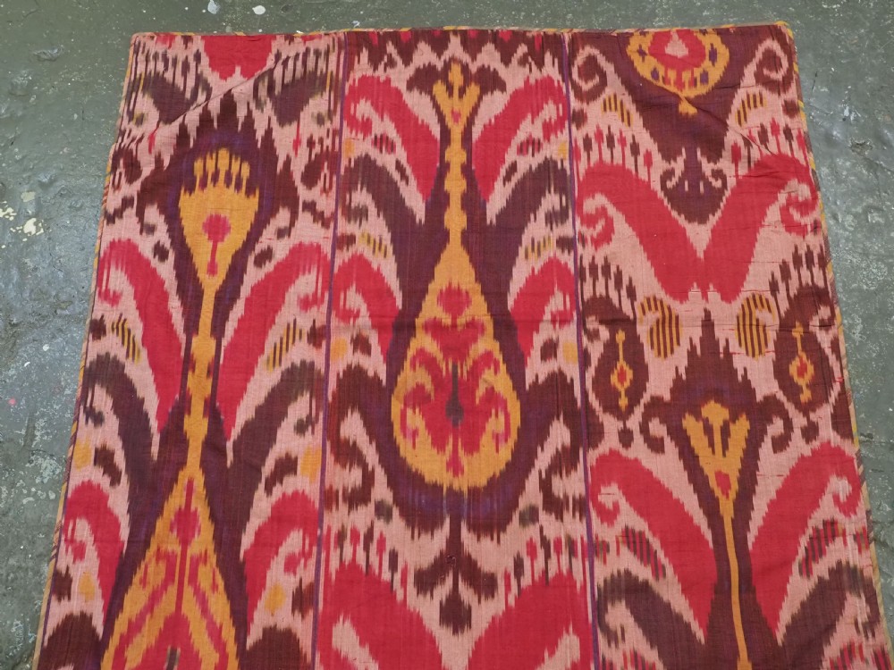 A rectangular handwoven Central Asian textile displaying vibrant geometric ikat motifs in crimson, yellow, and deep purple across three vertically stitched panels. View III
