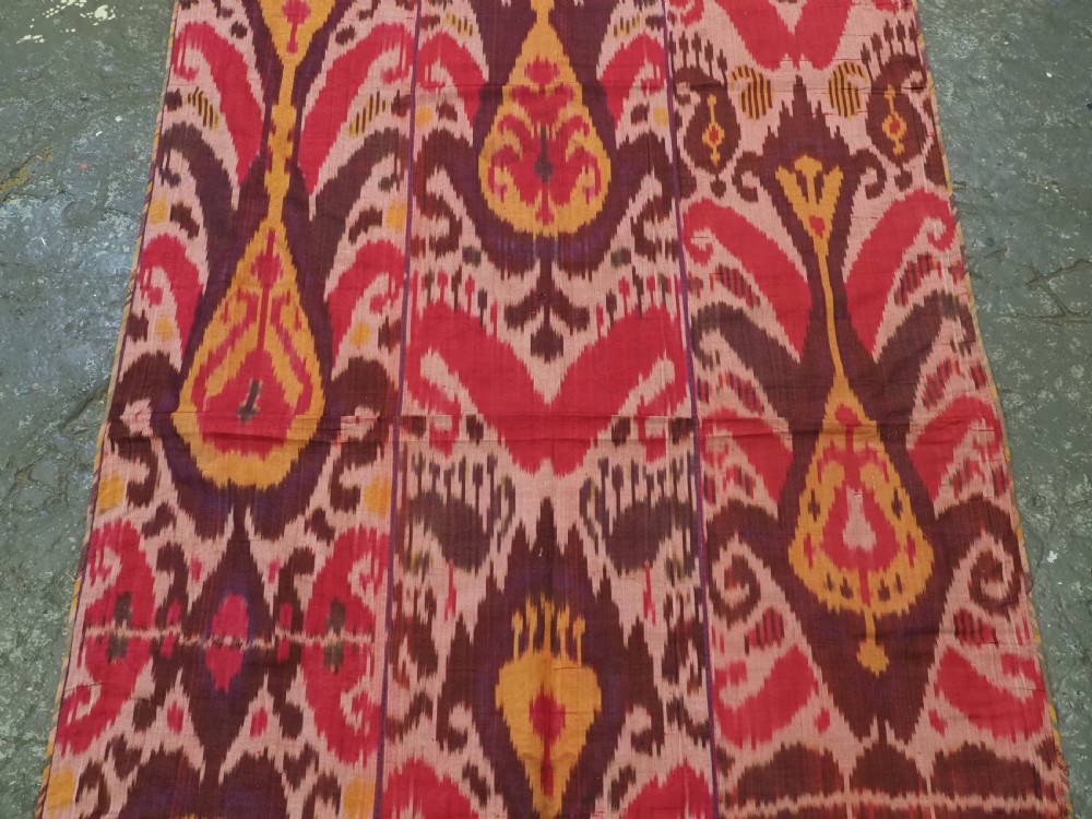 A rectangular handwoven Central Asian textile displaying vibrant geometric ikat motifs in crimson, yellow, and deep purple across three vertically stitched panels. View IV