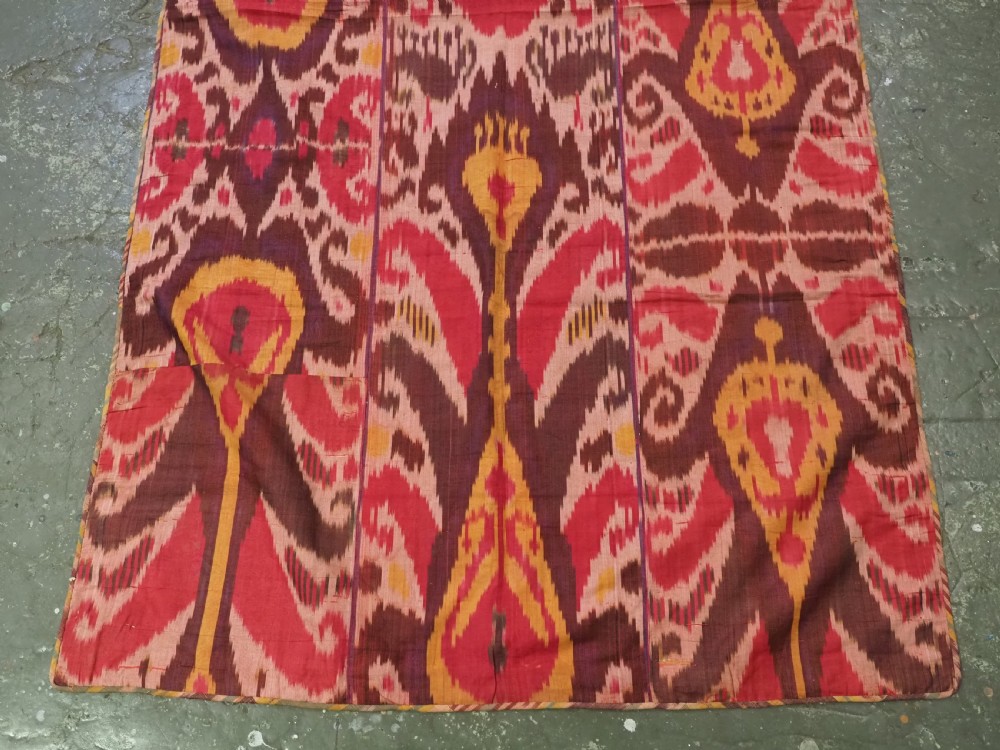 A rectangular handwoven Central Asian textile displaying vibrant geometric ikat motifs in crimson, yellow, and deep purple across three vertically stitched panels. View V