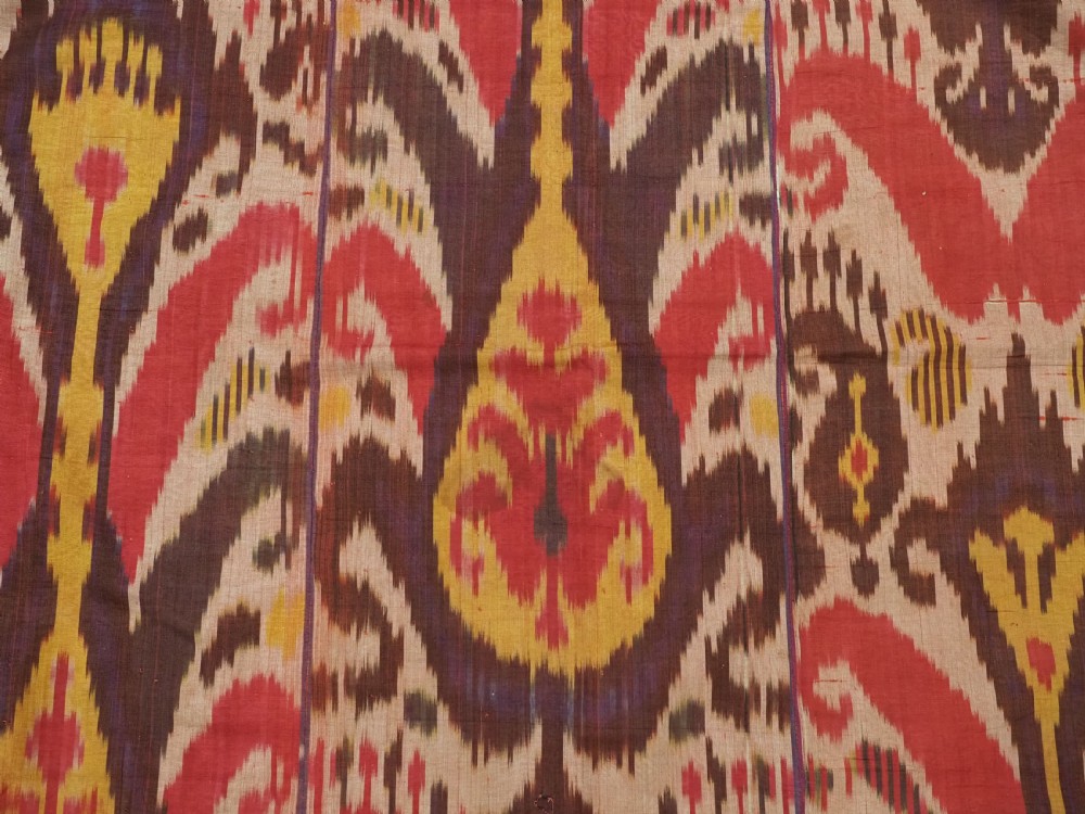 A rectangular handwoven Central Asian textile displaying vibrant geometric ikat motifs in crimson, yellow, and deep purple across three vertically stitched panels. View VI
