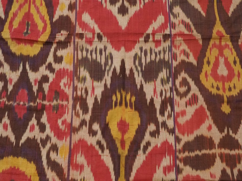 A rectangular handwoven Central Asian textile displaying vibrant geometric ikat motifs in crimson, yellow, and deep purple across three vertically stitched panels. View VII