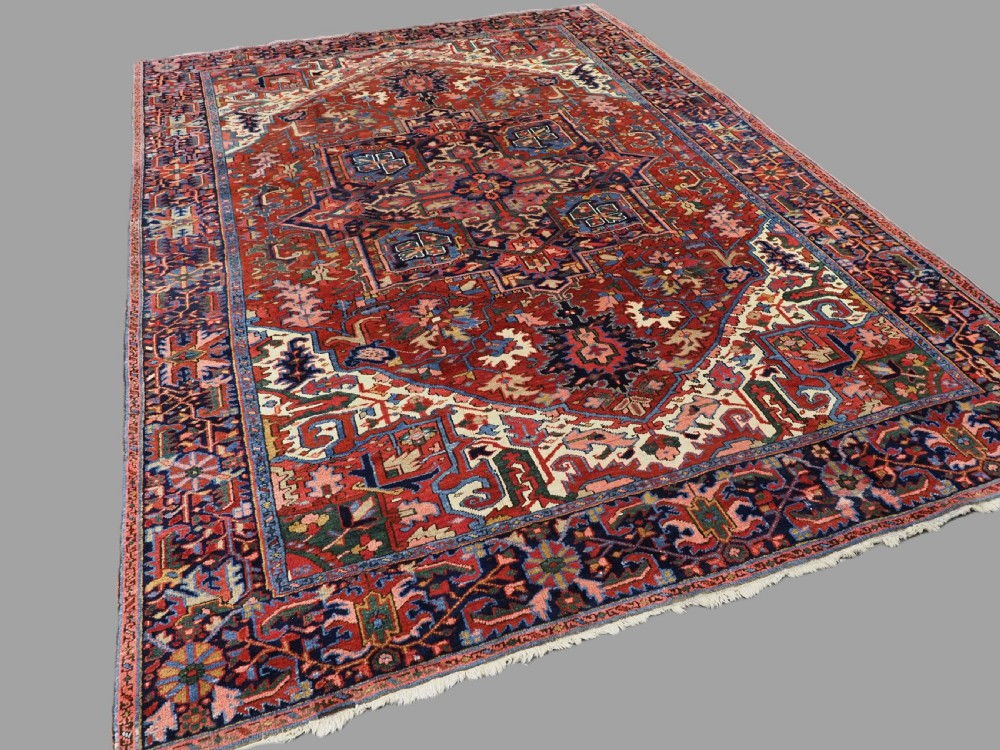 An antique hand-knotted Persian Heriz wool carpet featuring a central geometric medallion, angular spandrels, a terracotta red field, and navy blue borders. View II