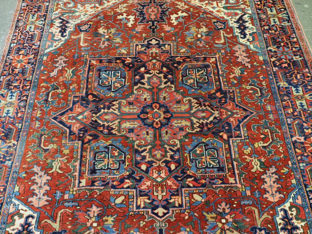 An antique hand-knotted Persian Heriz wool carpet featuring a central geometric medallion, angular spandrels, a terracotta red field, and navy blue borders. View III