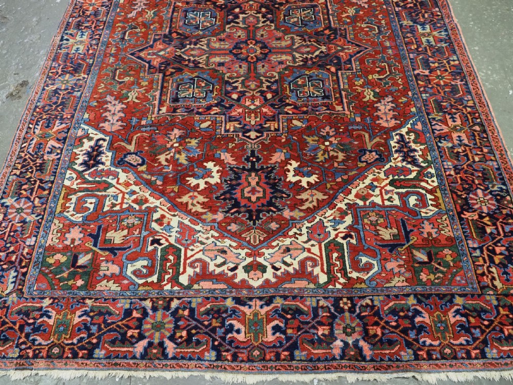 An antique hand-knotted Persian Heriz wool carpet featuring a central geometric medallion, angular spandrels, a terracotta red field, and navy blue borders. View IV