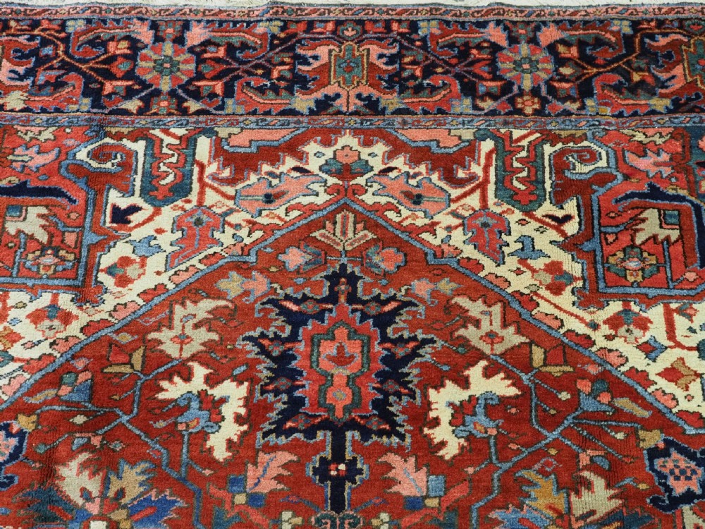 An antique hand-knotted Persian Heriz wool carpet featuring a central geometric medallion, angular spandrels, a terracotta red field, and navy blue borders. View VII