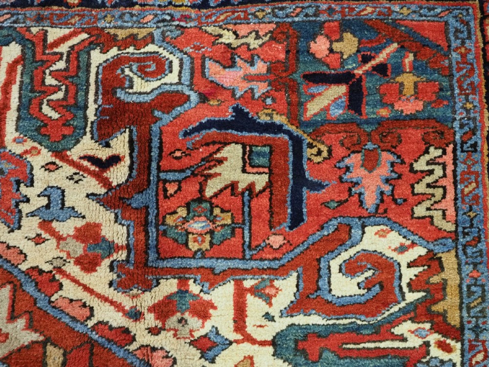 An antique hand-knotted Persian Heriz wool carpet featuring a central geometric medallion, angular spandrels, a terracotta red field, and navy blue borders. View VIII