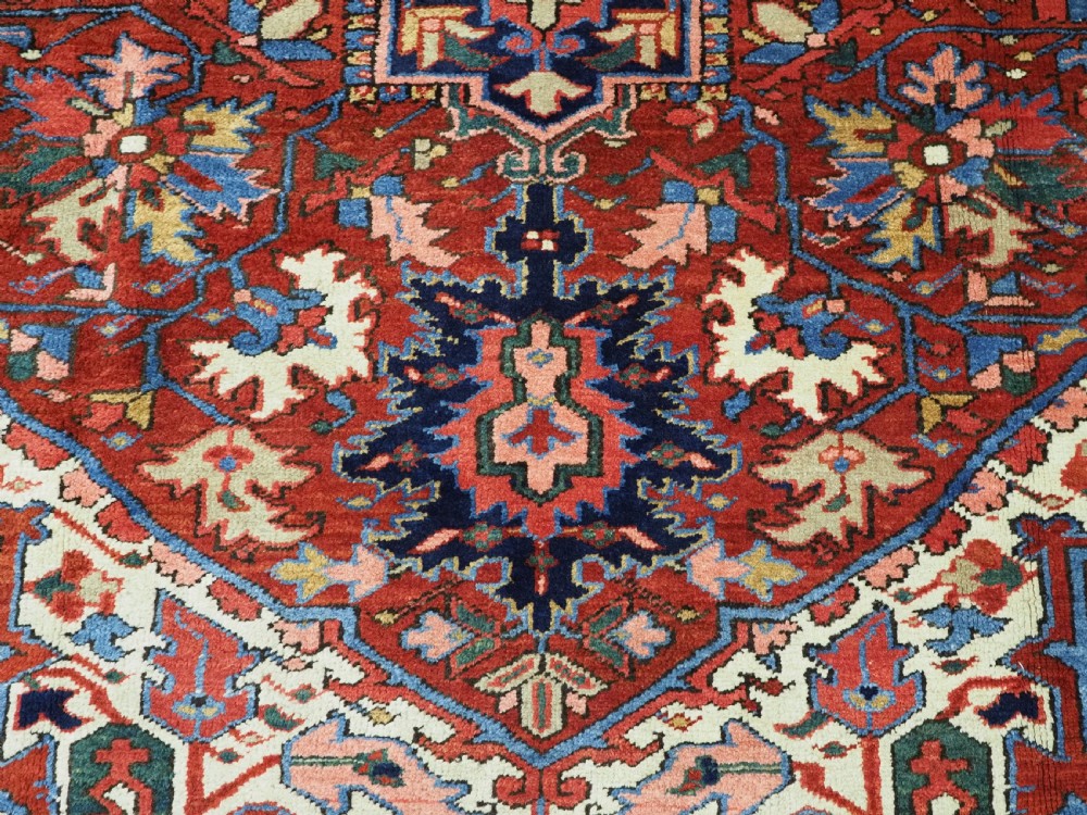 An antique hand-knotted Persian Heriz wool carpet featuring a central geometric medallion, angular spandrels, a terracotta red field, and navy blue borders. View X