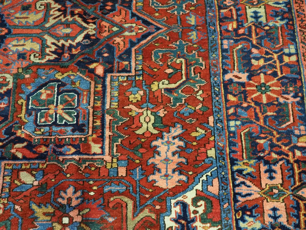 An antique hand-knotted Persian Heriz wool carpet featuring a central geometric medallion, angular spandrels, a terracotta red field, and navy blue borders. View XI